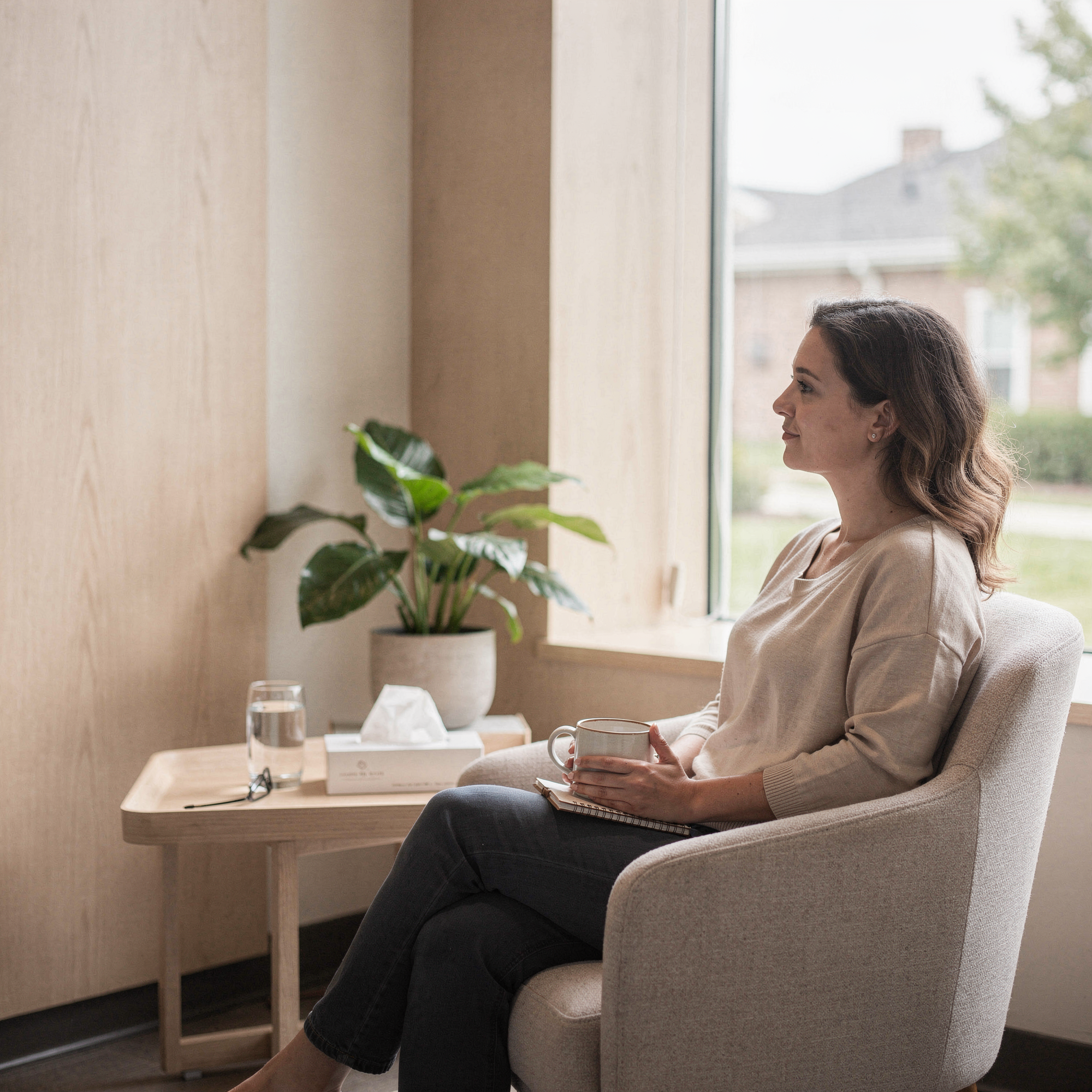 Woman sitting in a comfortable chair holding a cup of tea in a calm, light-filled psychiatric care consultation room